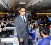 日本行きの航空機内で、サポーターにお礼をしながら歩を進める岡田監督